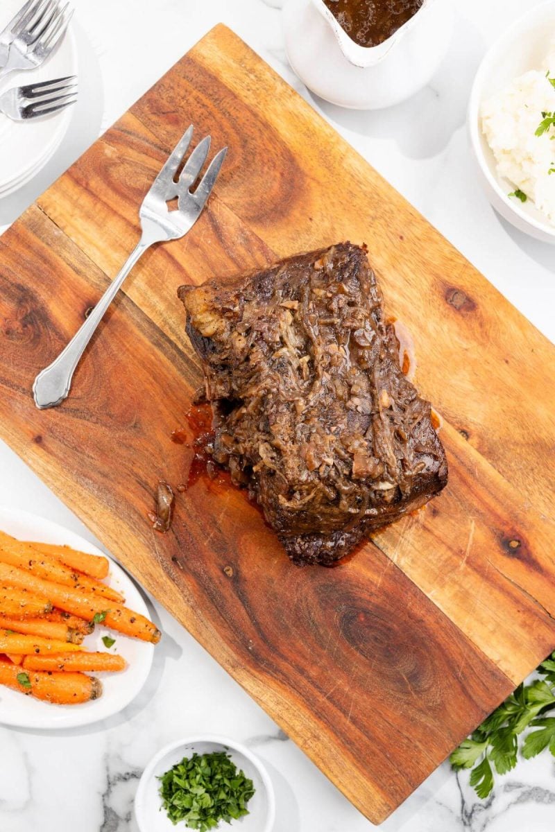 A whole cooked brisket is on a wooden board by side dishes.