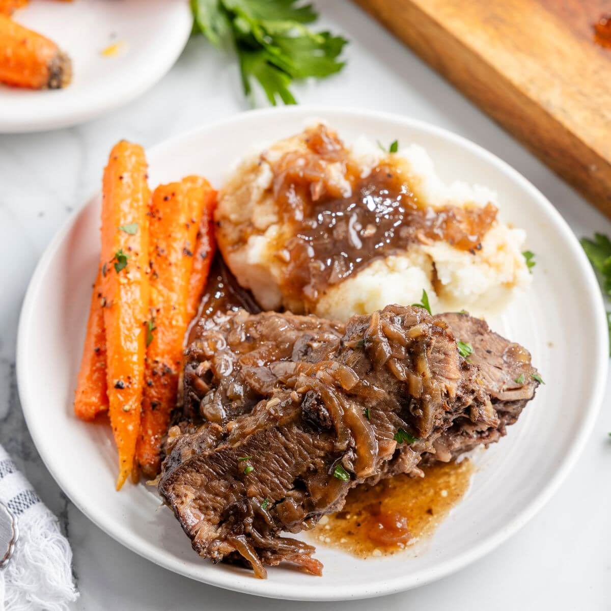 Brisket is served on a plate with mashed potatoes and gravy and carrots.