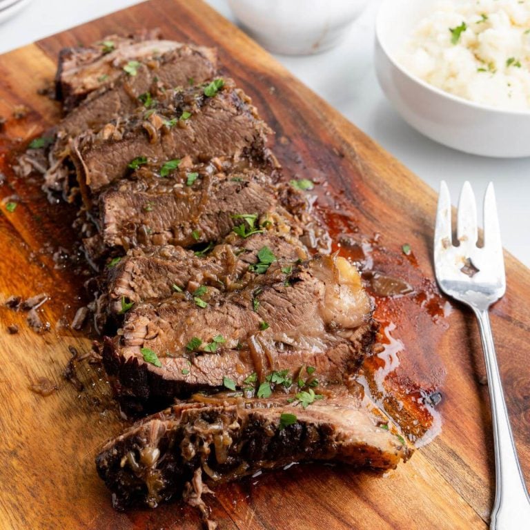 A row of brisket slices on a wooden board are served next to mashed potatoes.