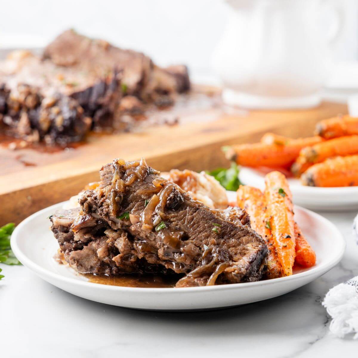 Meat with gravy and cooked carrots are shown next to full board of brisket and carrots.