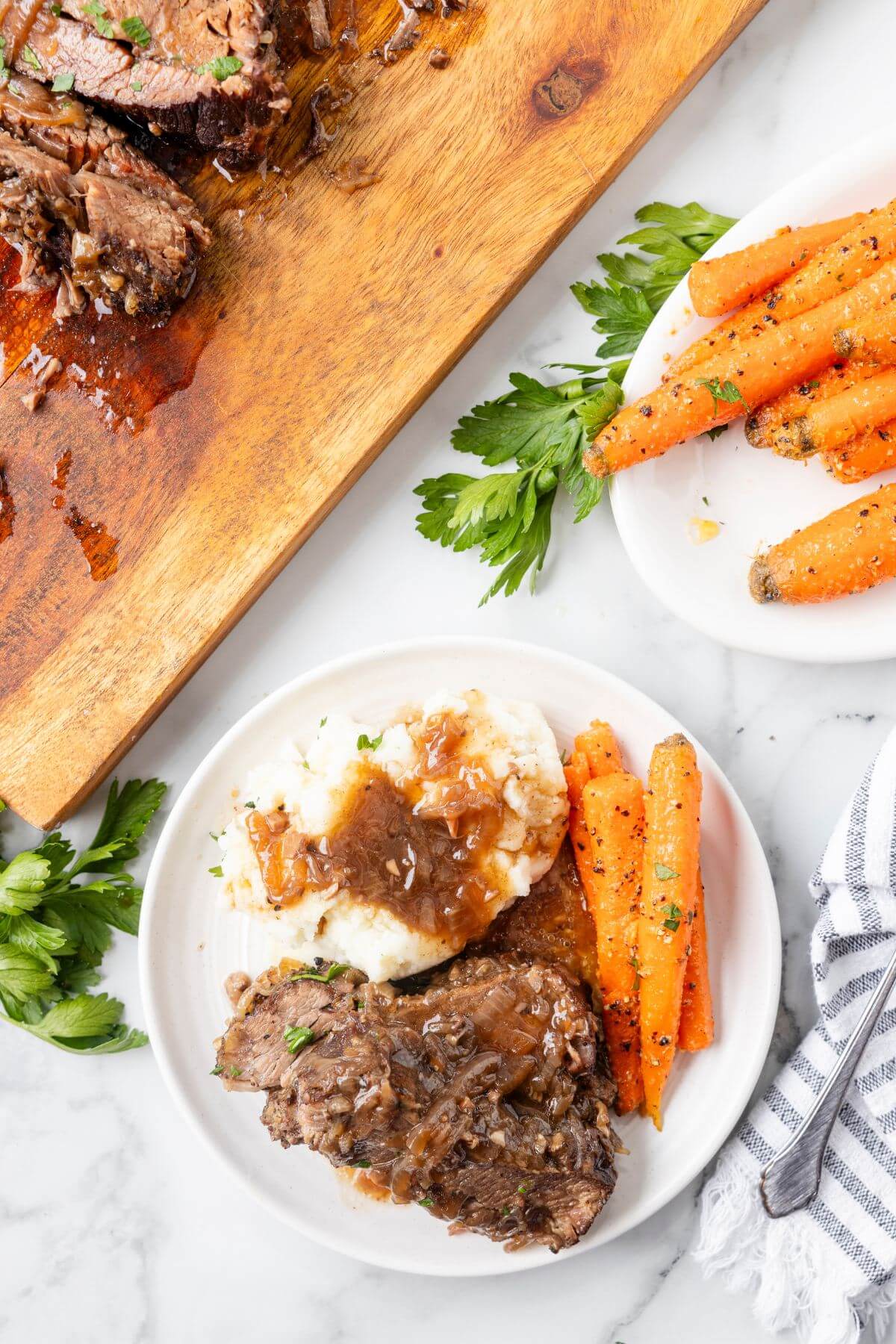 Cooked carrots and brisket are served alongside mashed potatoes and gravy.