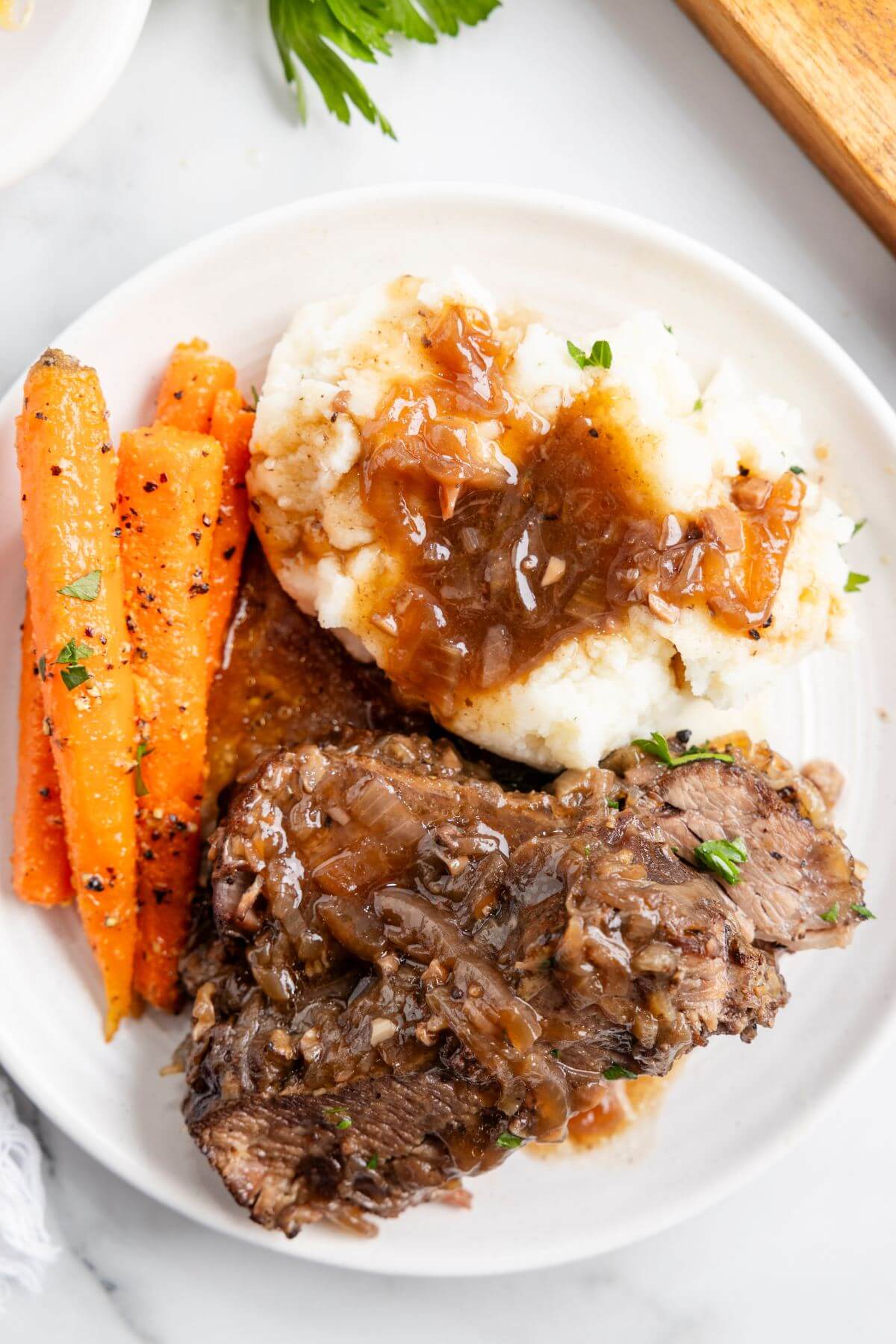 Mashed potatoes and gravy, glazed carrots, and brisket are served on a white plate.