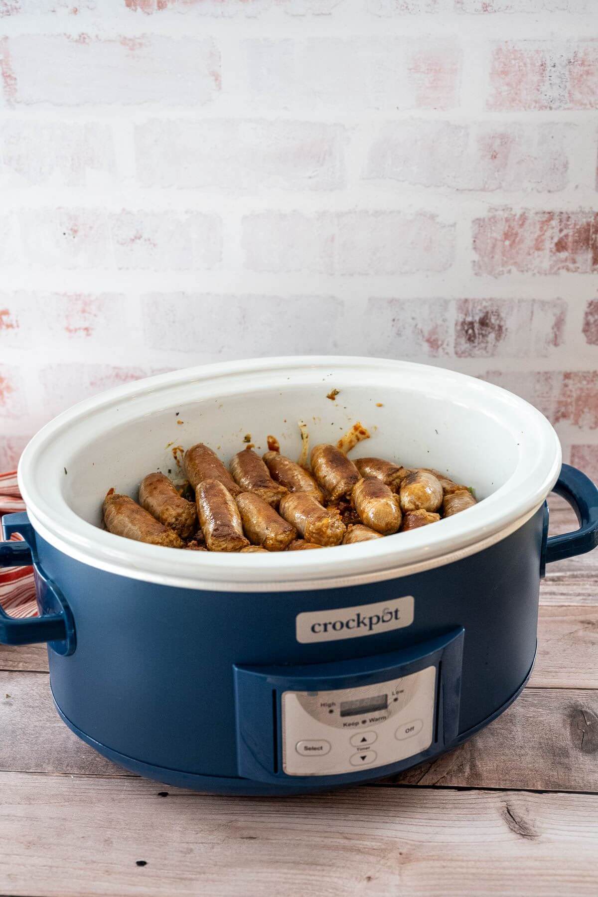 A blue crock pot with white top is shown from side where only sausages on top are showing.