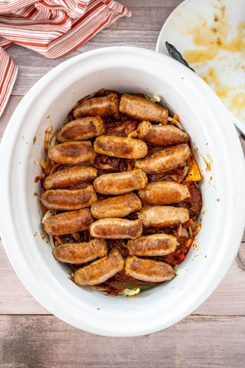 Browned sausages lay in rows on top of mixture in crock pot.