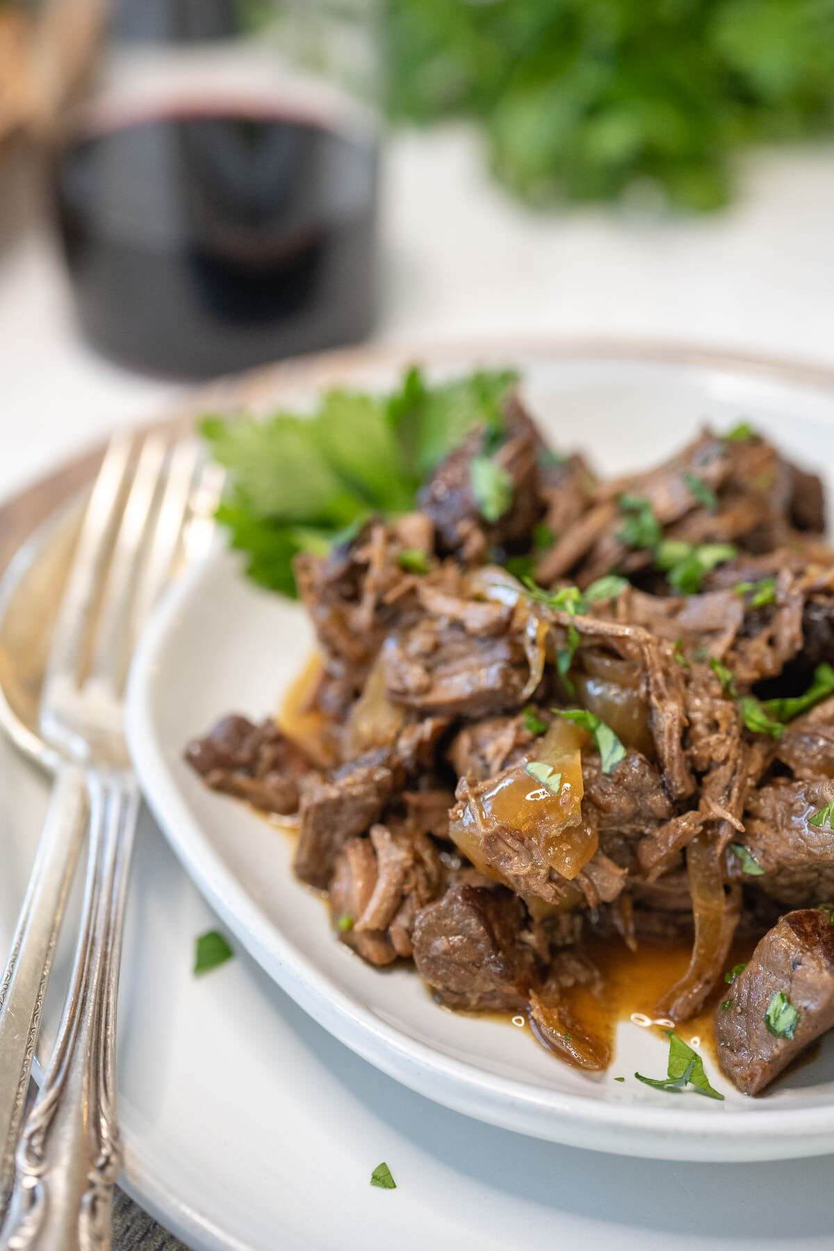 Browned steak bites cover a plate with silverware and wine nearby.