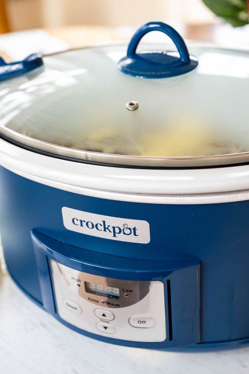 A blue crockpot is shown with its lid on and steamy.