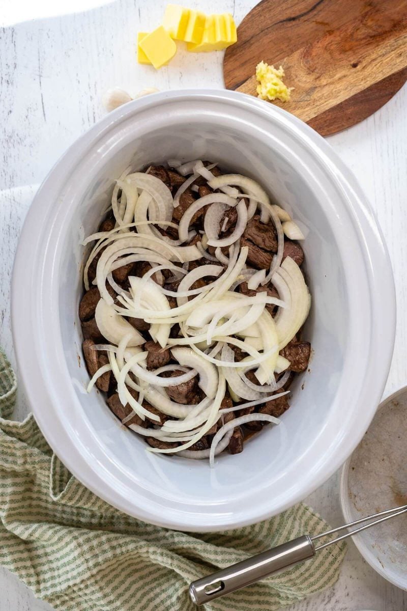 Raw onions cover steak in an open crock pot.