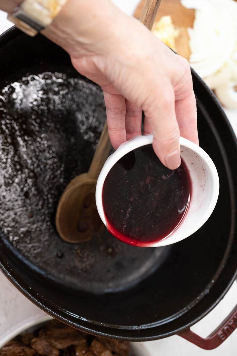 A hand pours red wine from bowl into pan.