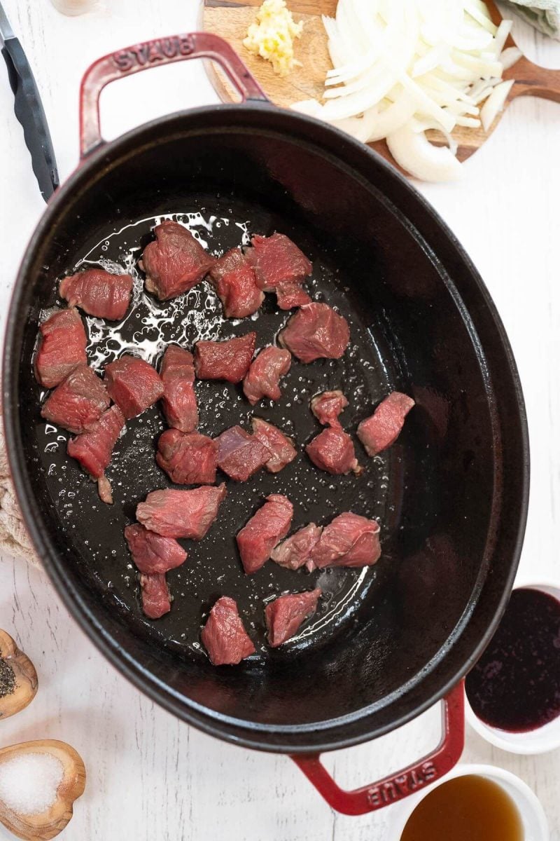 Raw steak bites sit in an oiled pan.