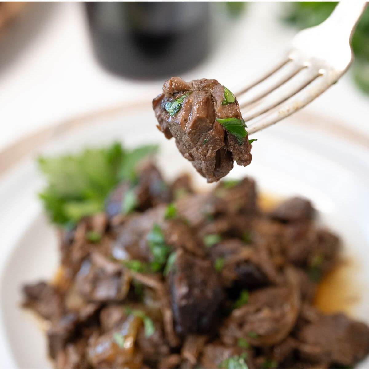 A fork raises up a steak tip and shows green garnish up close too.