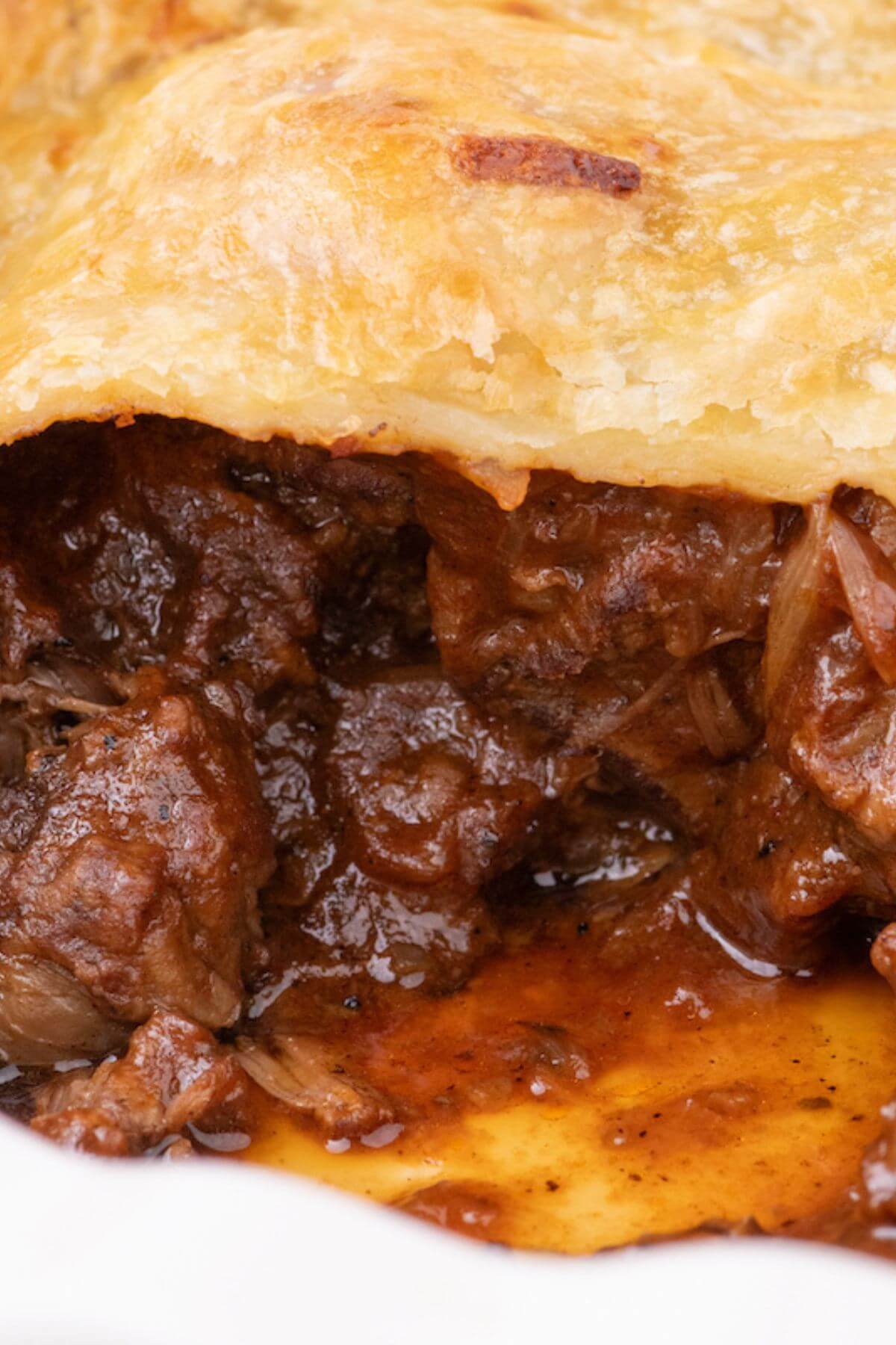 Close up of a tender and saucy, Steak and ale pie, oozing from under a cheddar puff pastry crust.