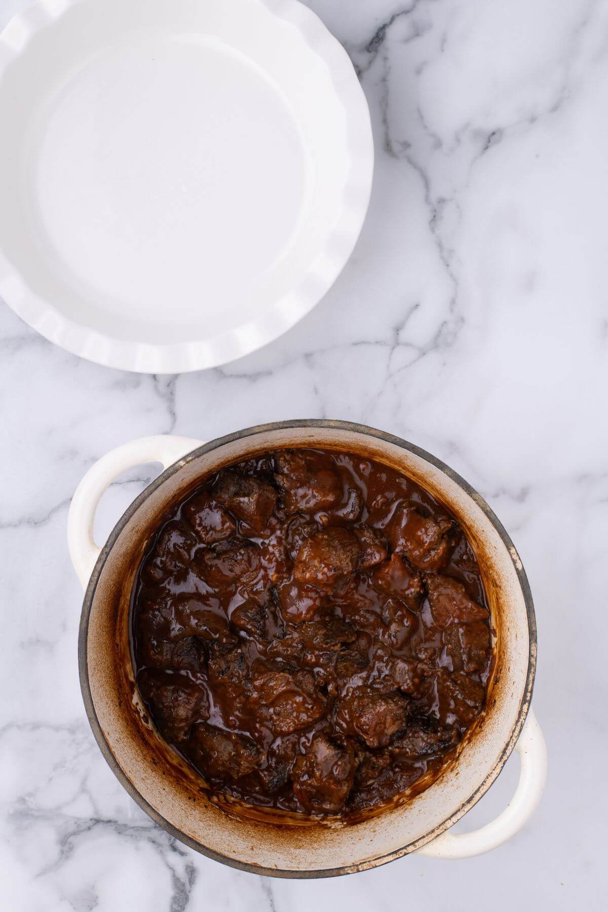 Cooked beef chunk mixture is in pot on a countertop.