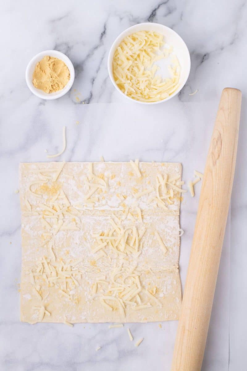 Cheese and mustard are sprinkled onto pastry sheet.