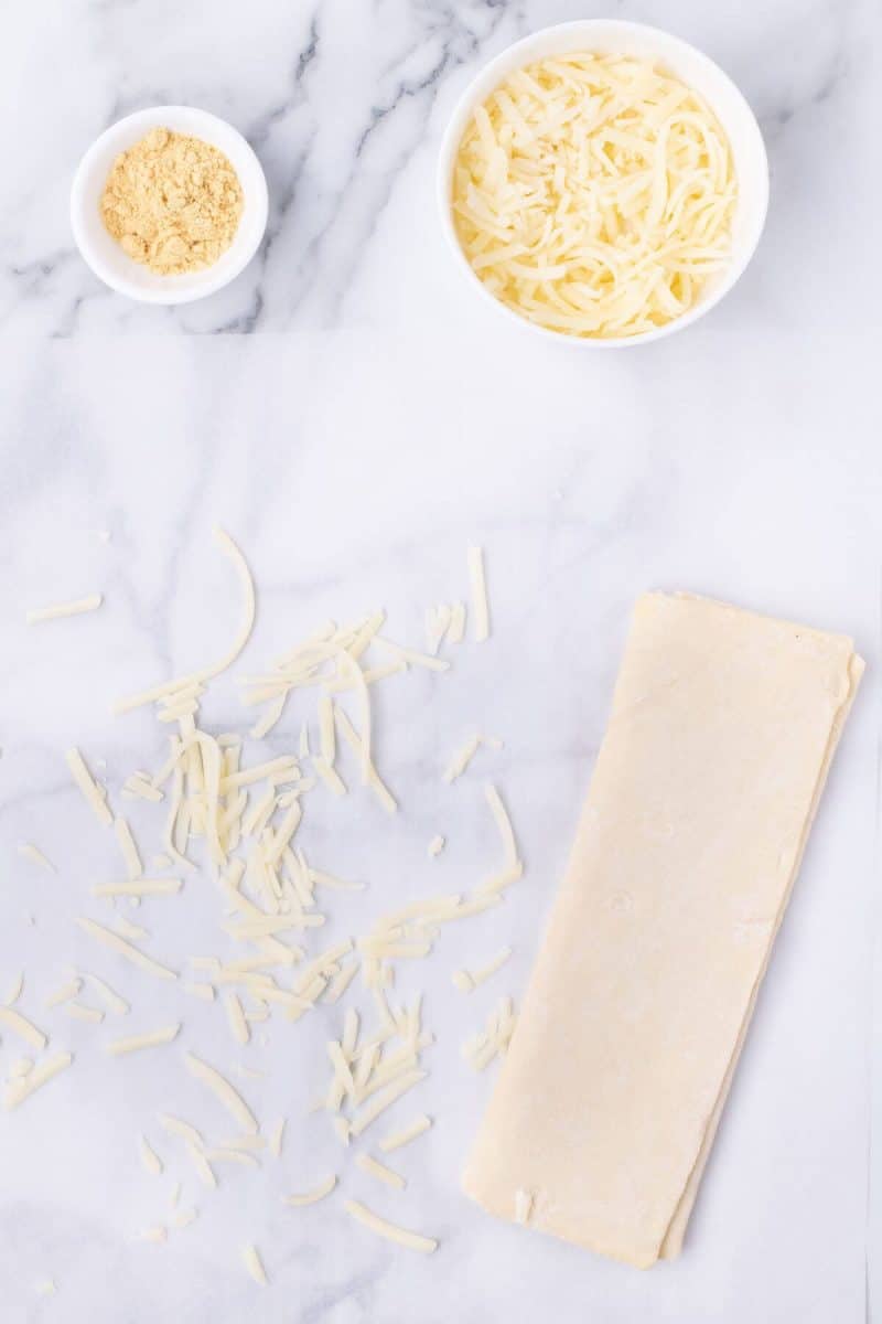Cheese is sprinkled on a counter next to bowls of other ingredients.