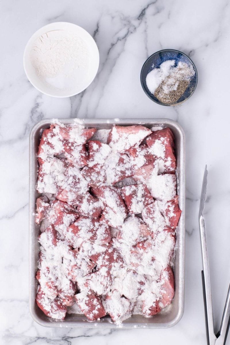 Raw meat is covered in flour in a pan.