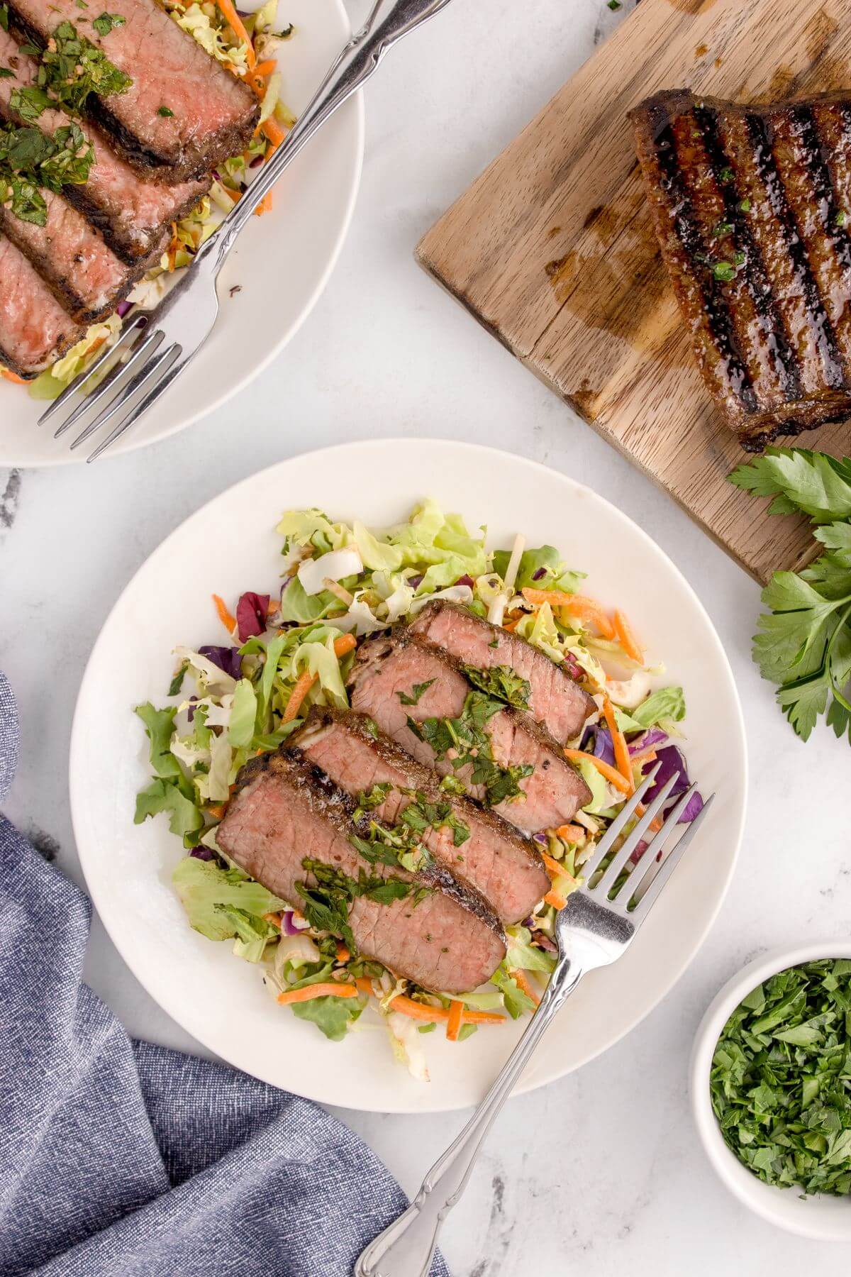 A table is full of plates of salad and steak.