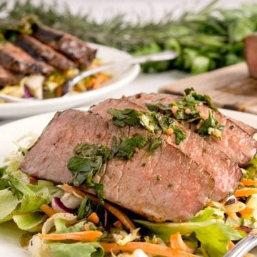 Steak slices are on a plate of salad surrounded by more greens.