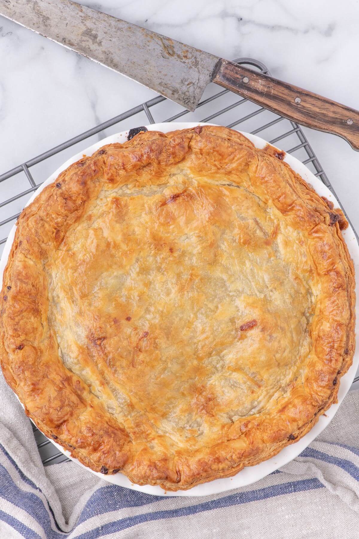 A Pub-style pie cools on a wire rack next to a knife.