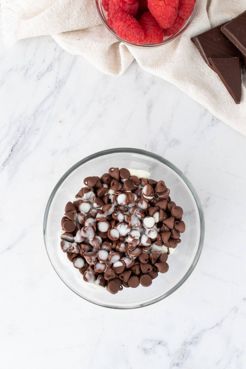 Chocolate chips with white ingredients on top sit in a glass bowl.
