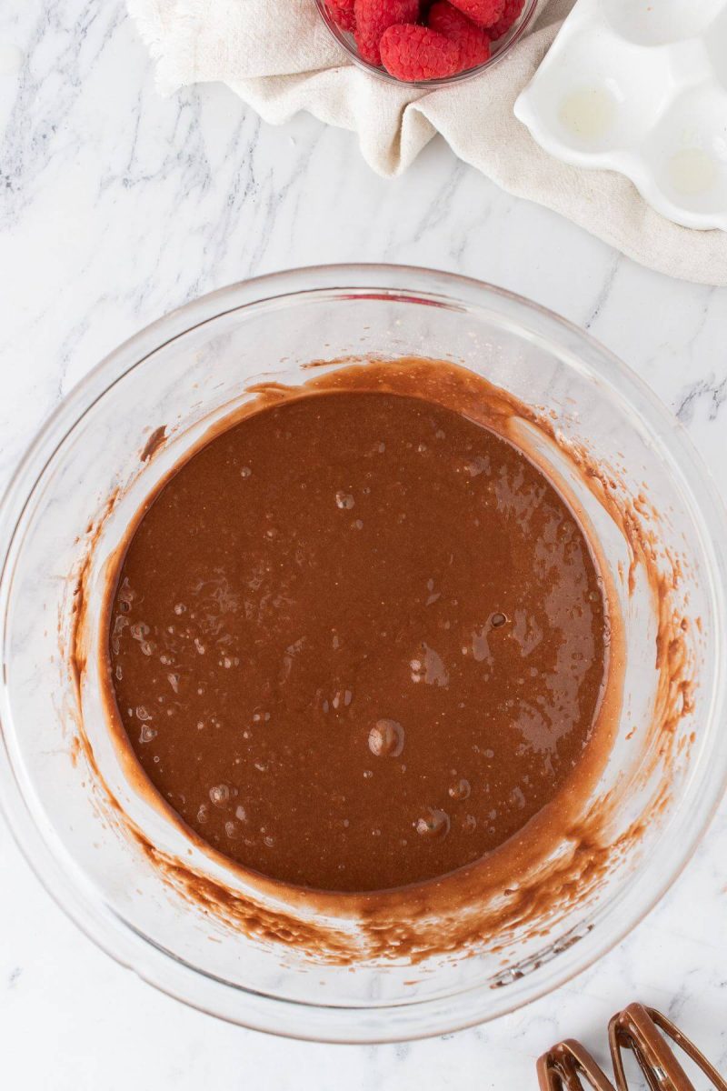 A glass bowl of mixed chocolate batter is next to beaters.