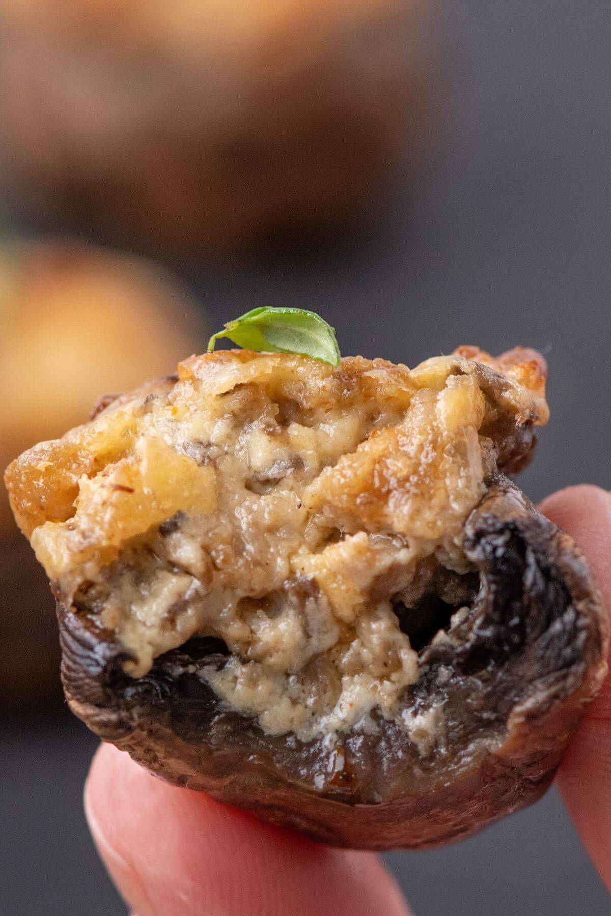 Two fingers hold up a stuffed mushroom close enough to see all the filling.