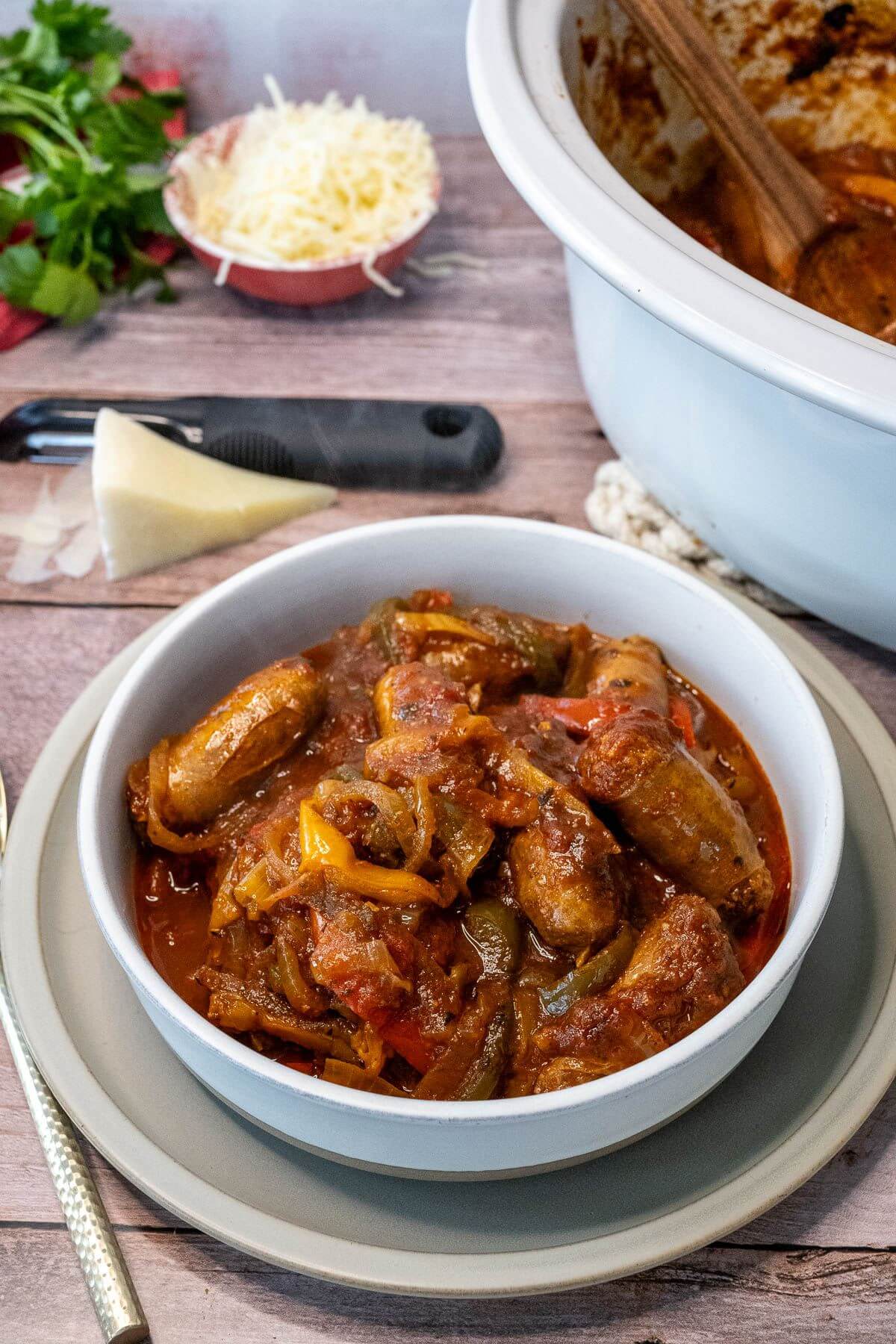 A bowl full of Italian sausages and peppers next to some cheese.