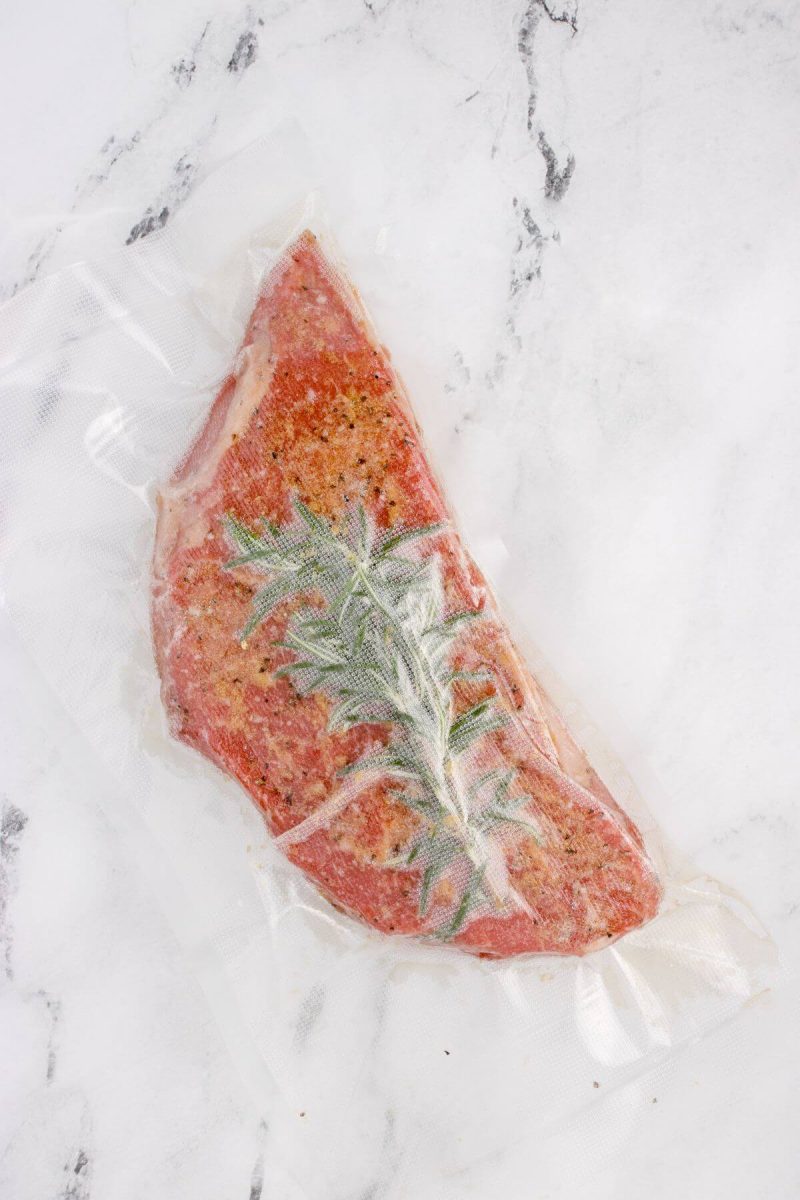 Plastic covers the cooked meat and rosemary with pockets of air around.