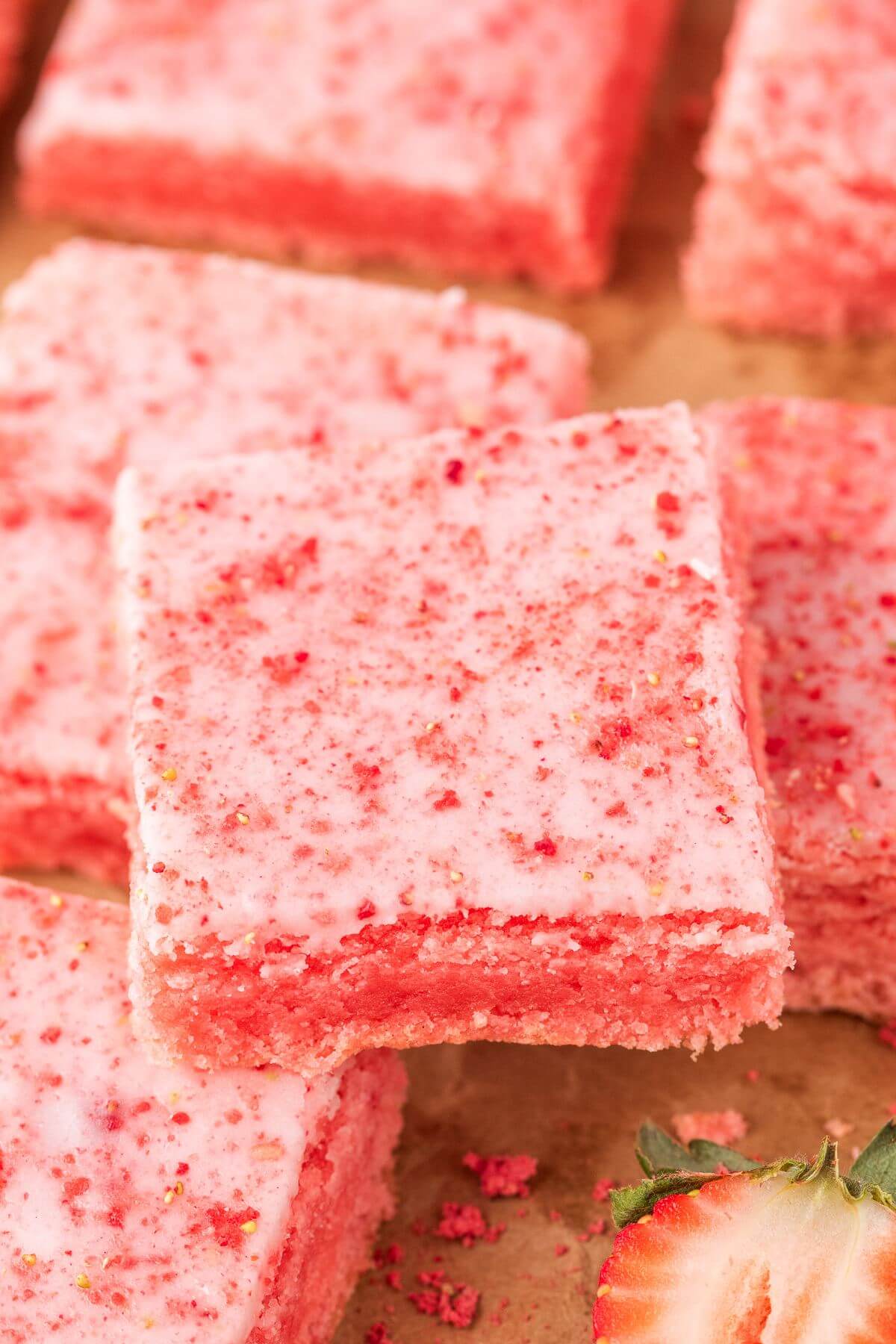 Pink strawberry blondies are in a row on a paper surface.