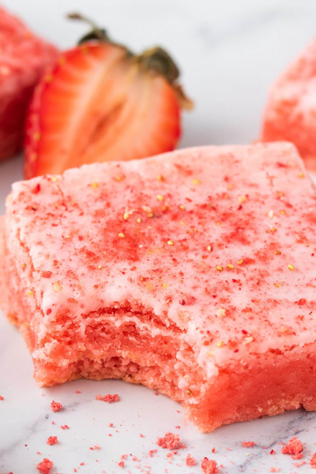 Strawberries lay behind a pink baked square with a bite taken from it.