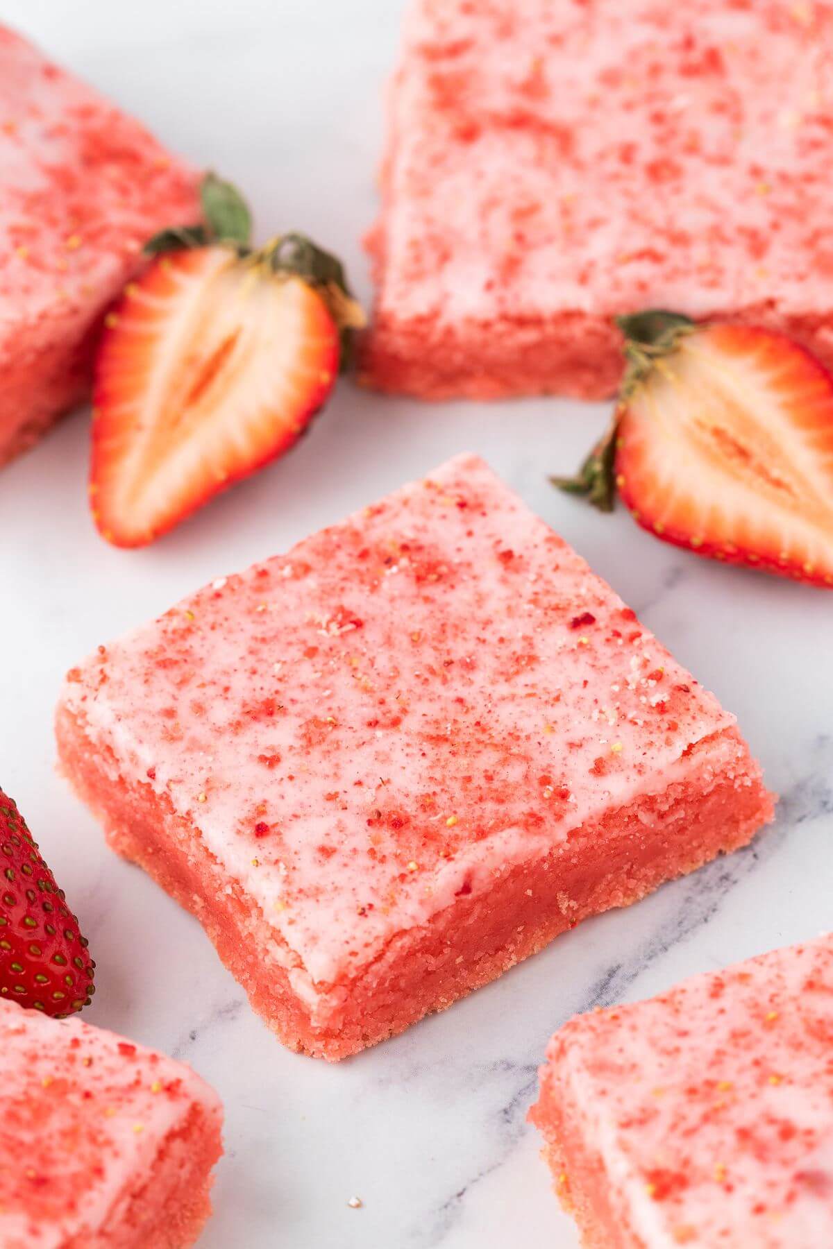 Strawberry pink brownies are scattered amongst strawberry halves on the counter.