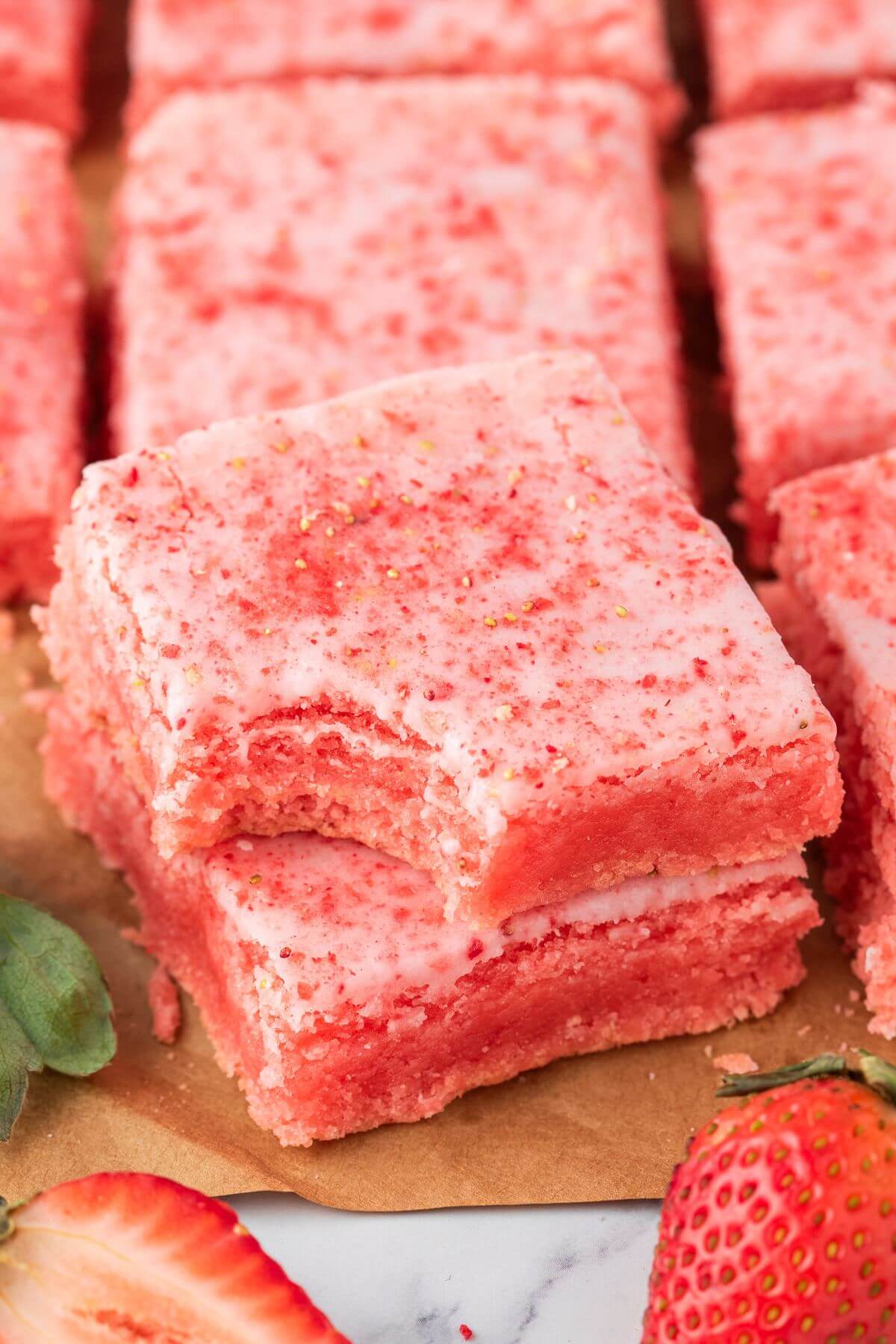 Two pink baked squares of strawberry brownies are stacked with a bite taken from top. one.