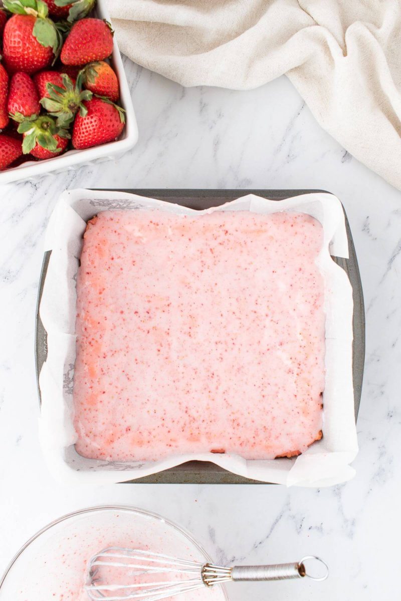 Light pink cake frosting fills a lined cake pan.