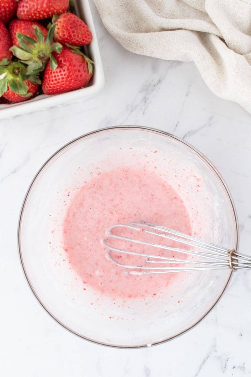 A light pink liquid is being stirred by whisk in bowl.