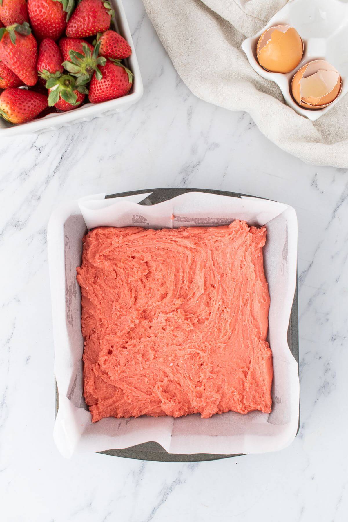 Pink cake batter is swirled into cake pan.