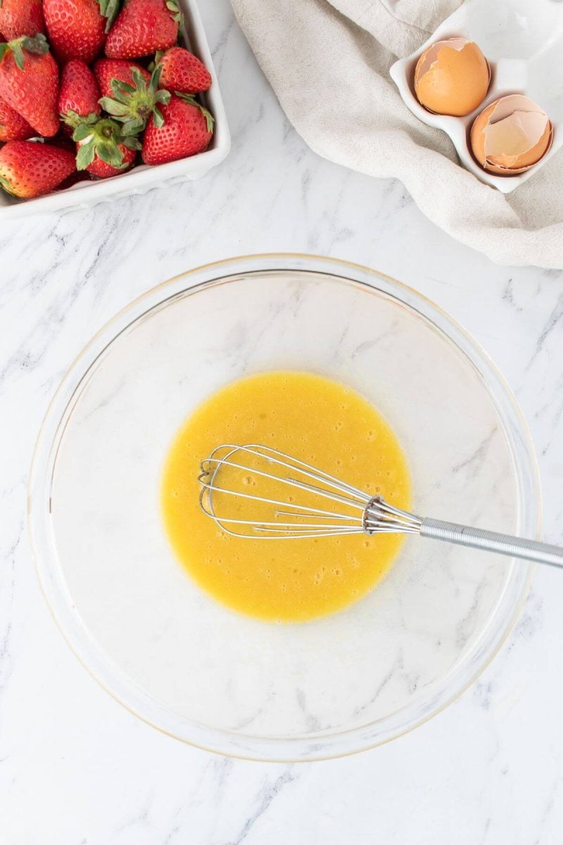 A whisk mixes the egg mixture in a glass bowl.