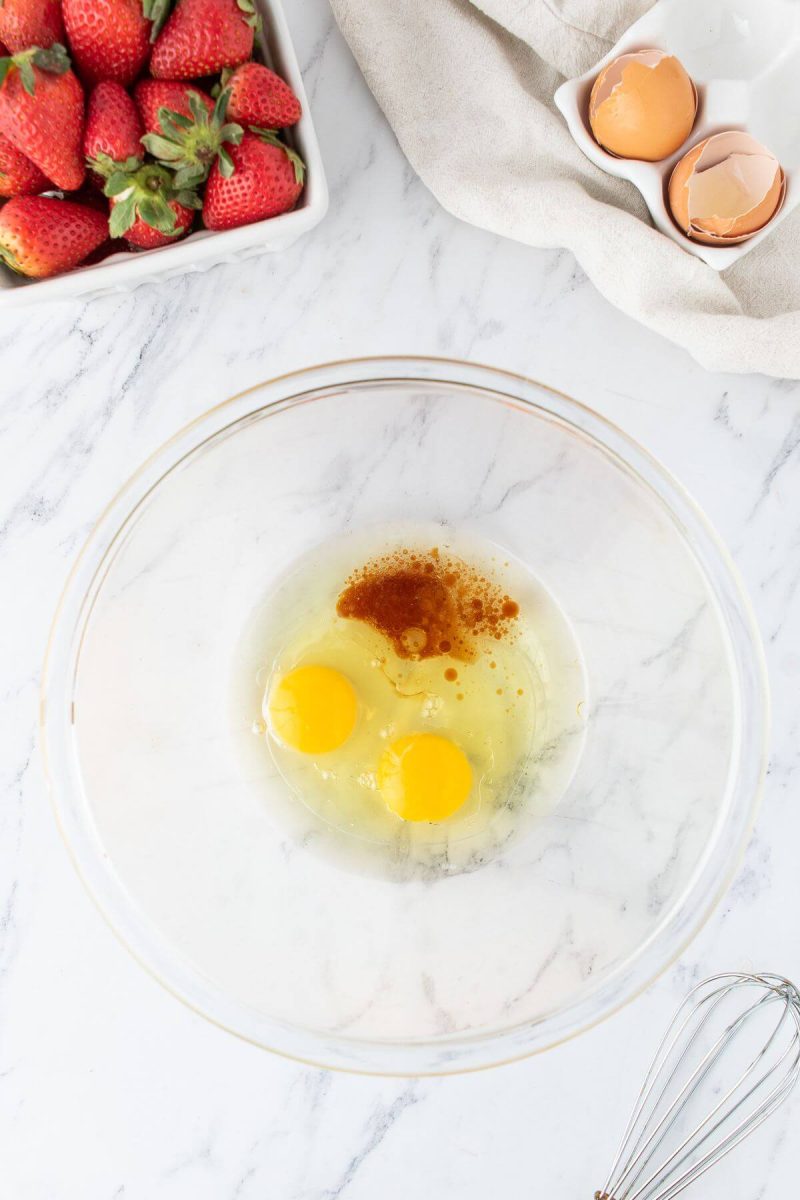 Eggs and vanilla are in a glass bowl for mixing.