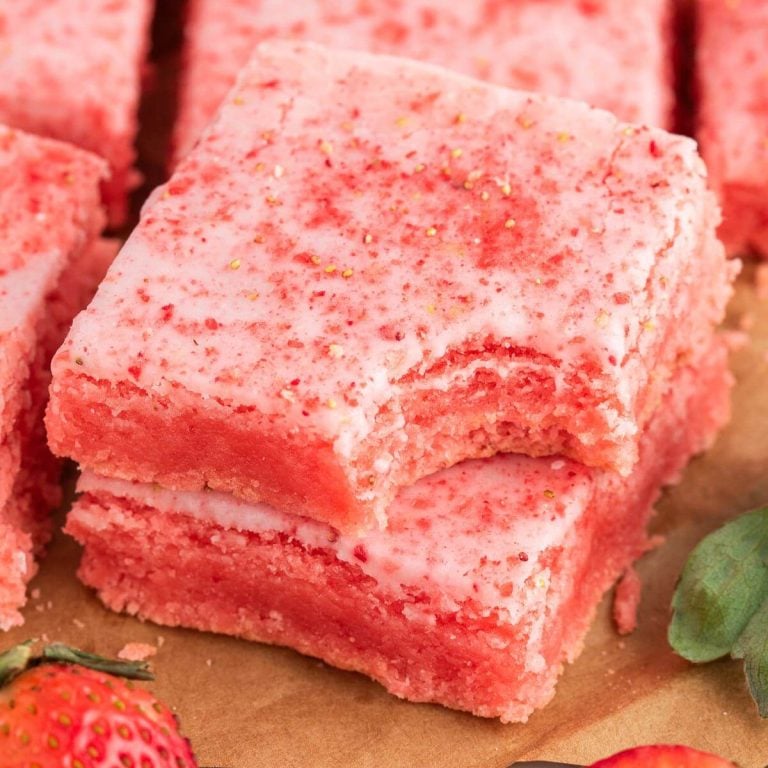 A stack of two pink brownies sits by strawberries on a paper sheet.