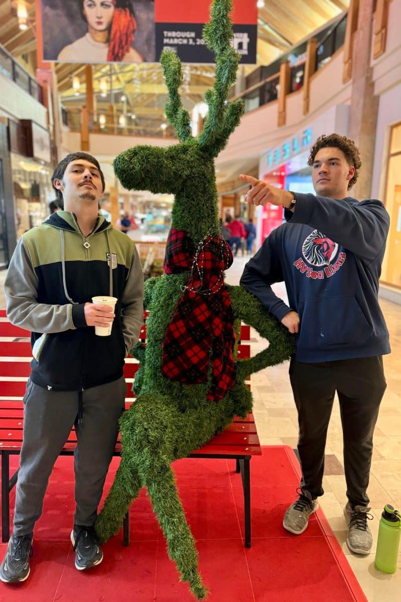 Silliness at the mall, two men standing next to a sitting reindeer. 