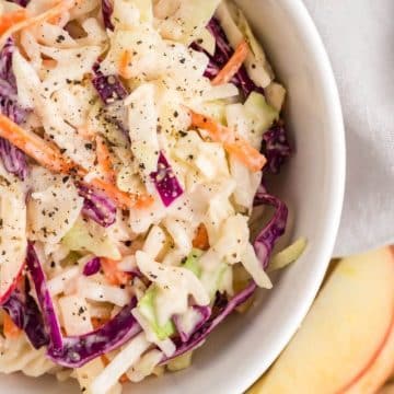 Seasoning tops a bowl of coleslaw served next to apple slices.