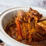 Sausage and peppers on a wooden spoon from a crockpot.