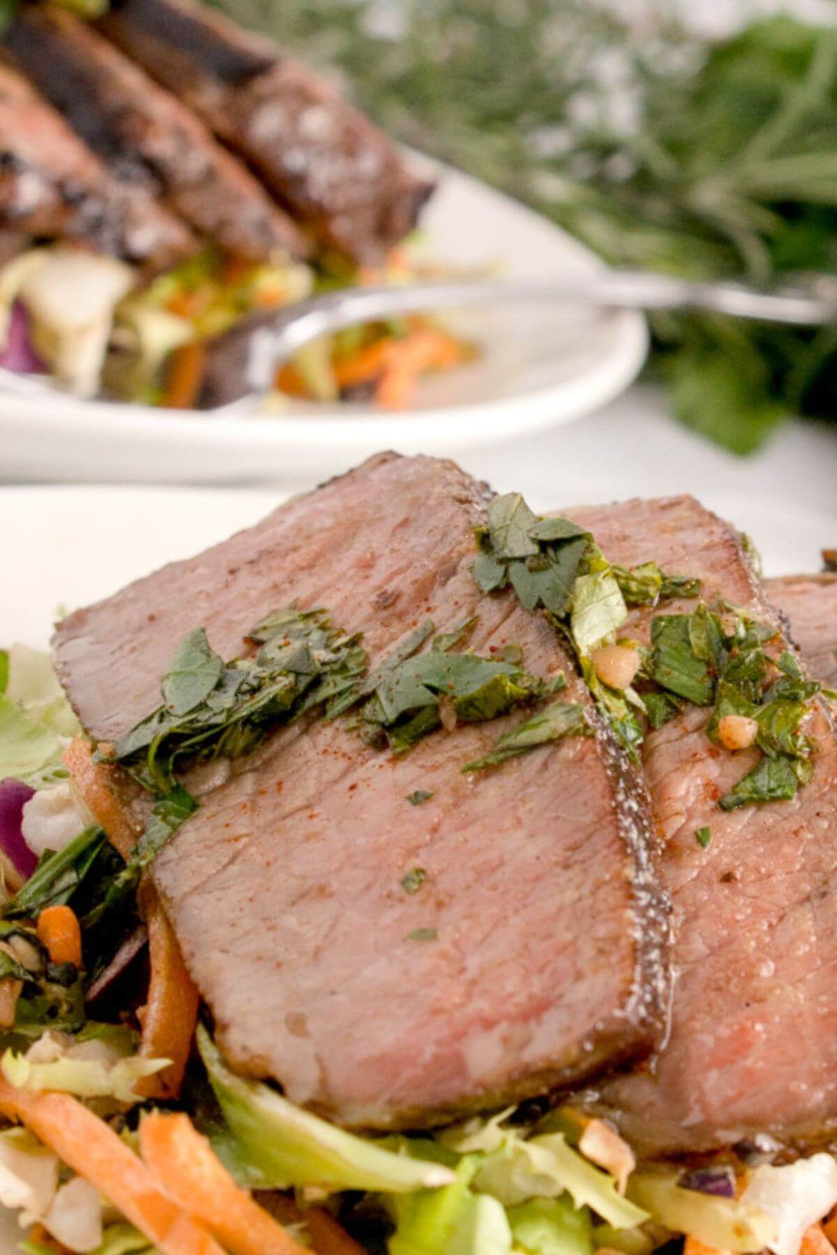 Meat pieces are on a bed of salad in front of another plate of the same.