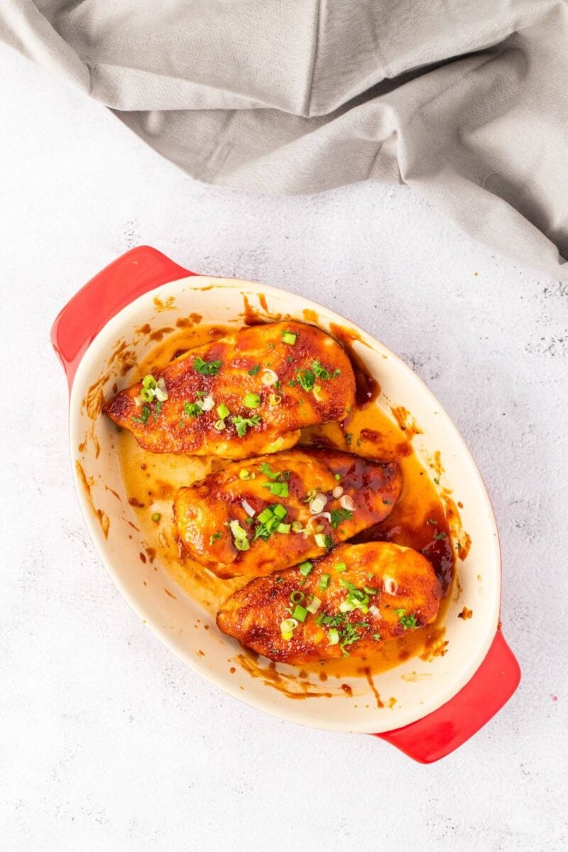 Three whole pieces of chicken are covered in barbecue sauce and green onions in dish.