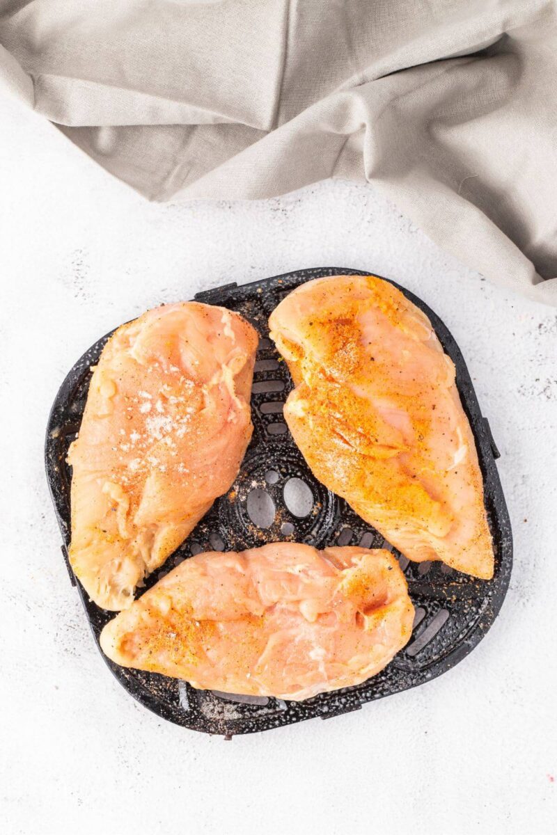 Partially cooked chicken breasts sit on air fryer basket.