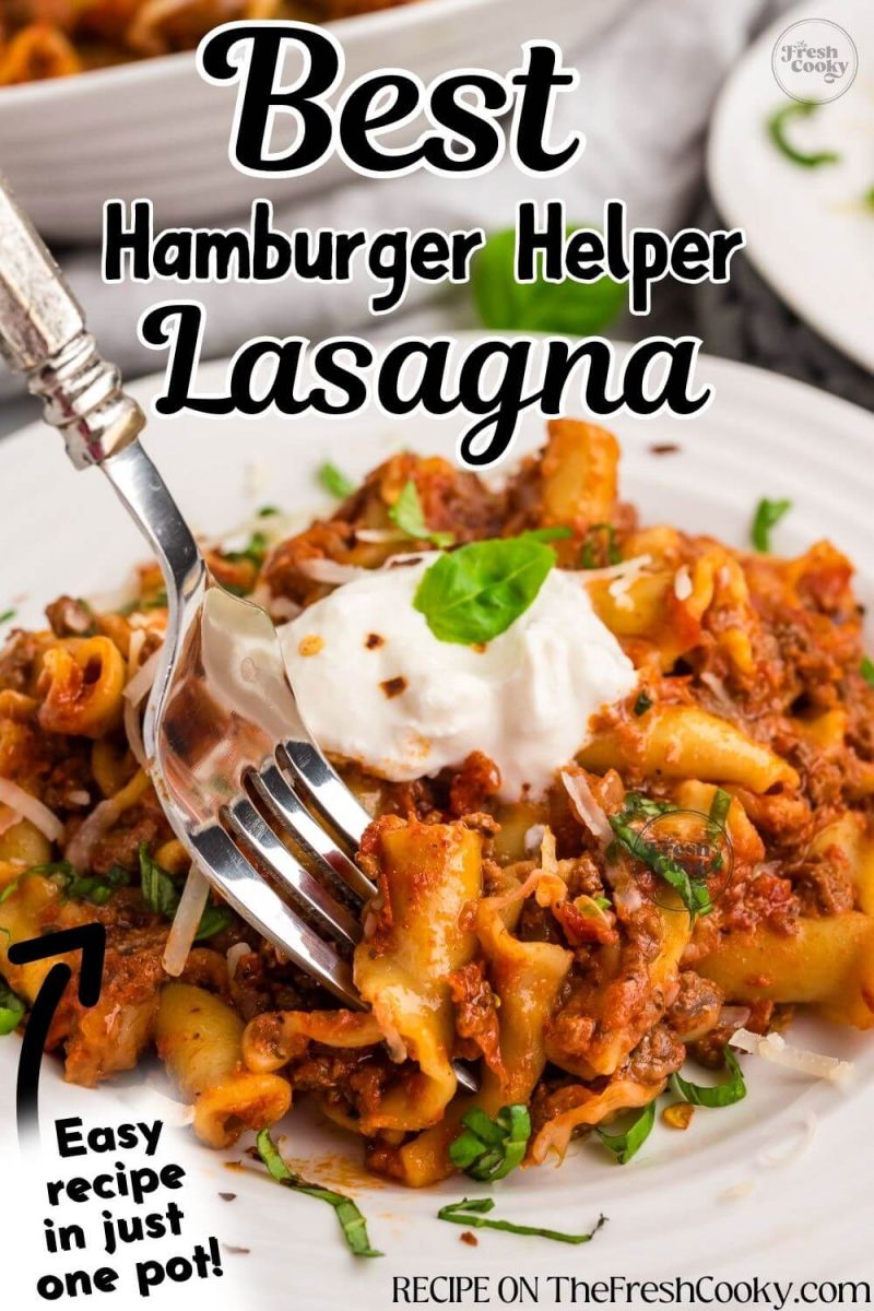 A fork dives into a pile of garnished lasagna mixture on plate, to pin.