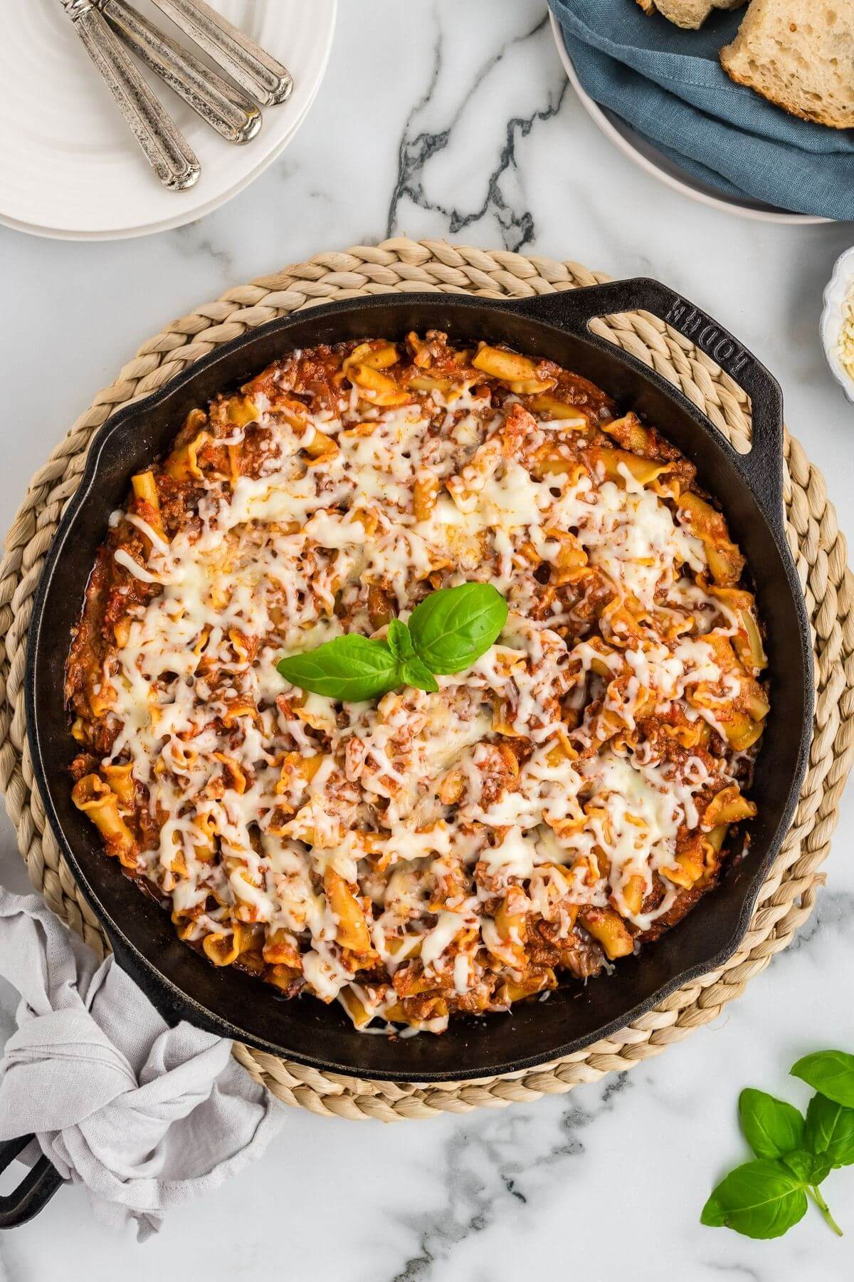 An iron pan is packed full of hamburger lasagna covered in cheeses with a sprig of greens in the center.
