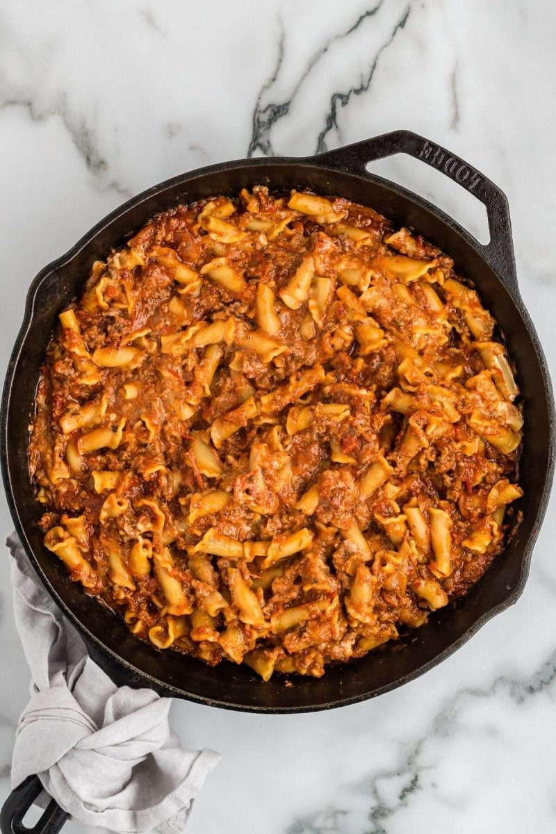 Tomato sauce, noodles, and meat sit in iron pan.