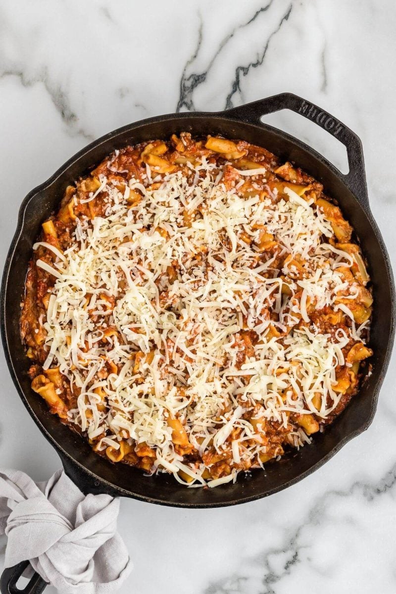 Unmelted white shredded cheese tops the lasagna noodle mixture in pan.