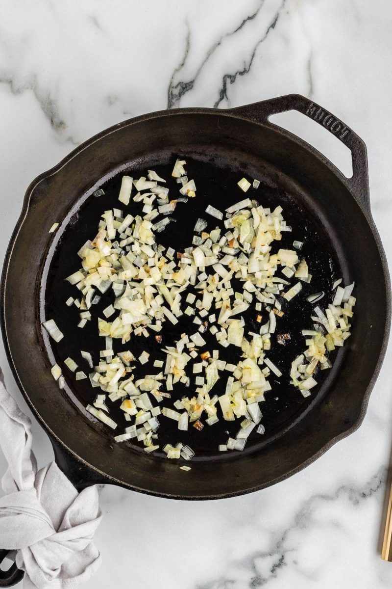 Minced onion pieces cook in oil in an iron pan.