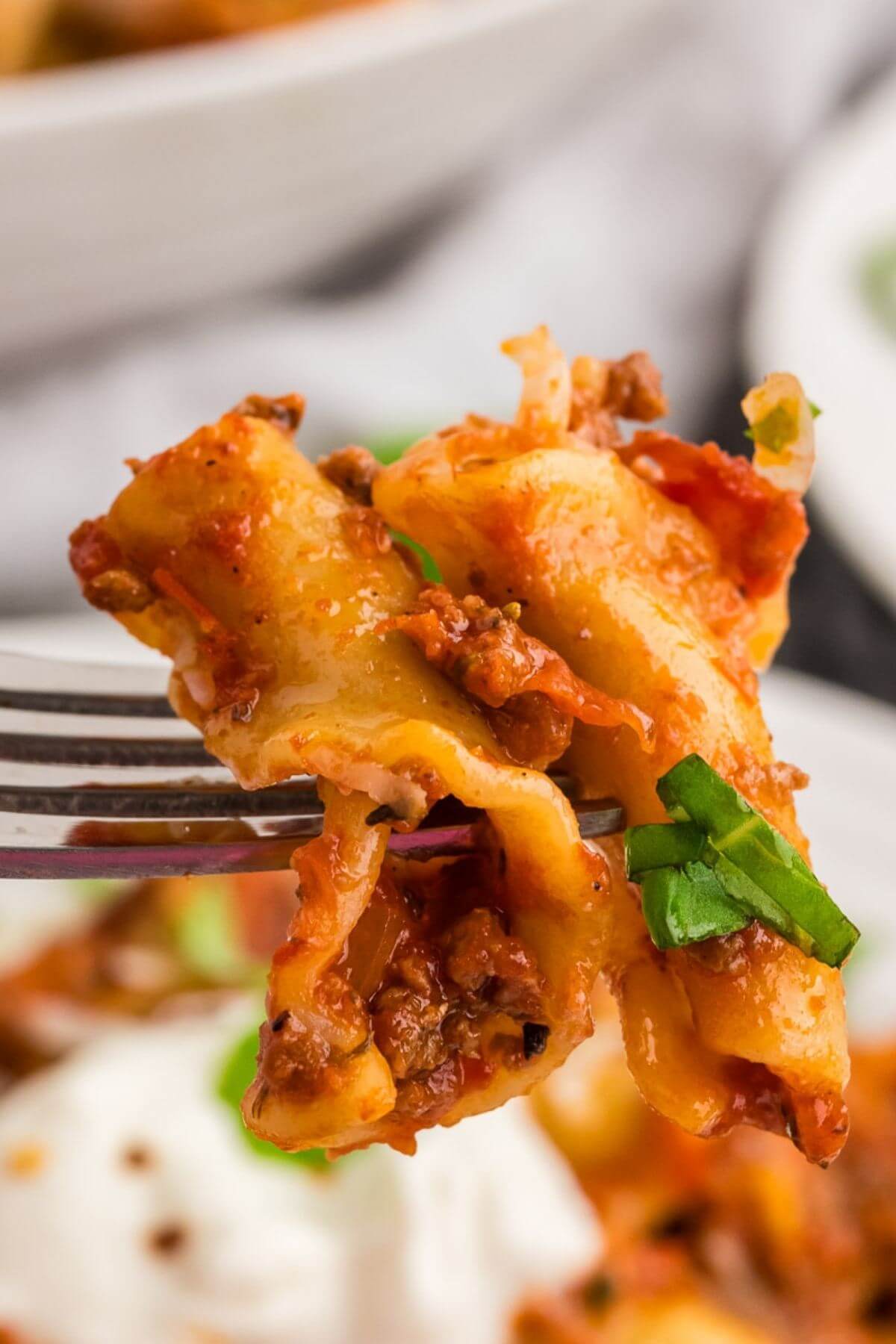 A fork holds up a couple of lasagna noodles showing the hamburger meat and greens up close.