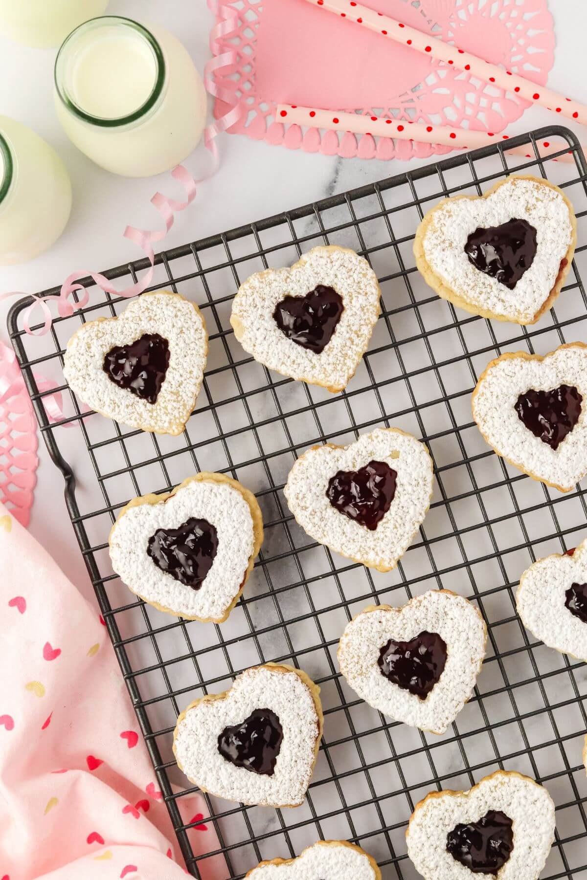 Heart cookies are in rows on a wire rack above pink decorations.